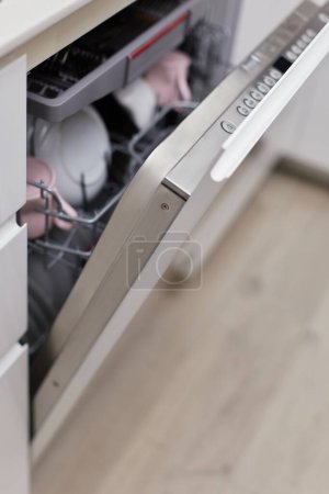 Photo for Open built-in dishwasher machine with clean cutlery, dishes, plates in white modern kitchen - Royalty Free Image
