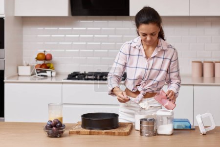 Téléchargez les photos : Jolie femme préparant la pâte pour tarte dans la cuisine moderne - en image libre de droit