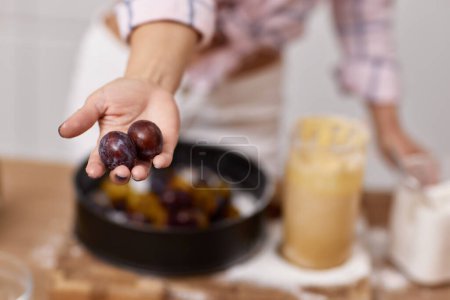 Photo for Female hand showing plums for preparing plum pie in light kitchen - Royalty Free Image