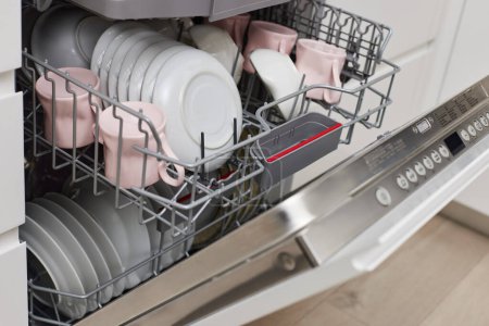 Téléchargez les photos : Machine à laver le vaisselle ouverte intégrée avec couverts propres, vaisselle, assiettes dans la cuisine moderne blanche - en image libre de droit
