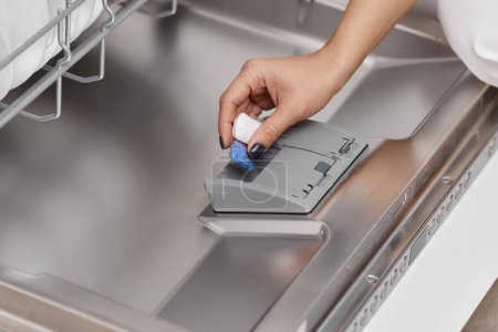 Photo for Female hand puts dishwasher tablet into open automatic built-in dishwasher machine. Close-up - Royalty Free Image
