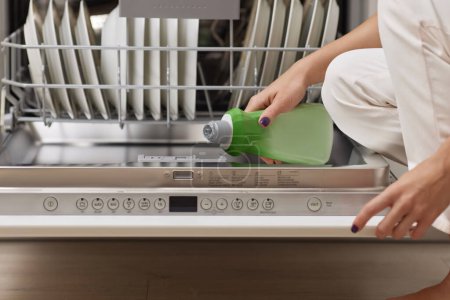 Foto de Mano femenina vierte ayuda de enjuague en el compartimiento del lavavajillas en la cocina blanca moderna - Imagen libre de derechos