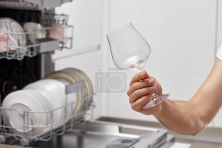 Téléchargez les photos : Main masculine prend des verres à vin du lave-vaisselle dans la cuisine. - en image libre de droit