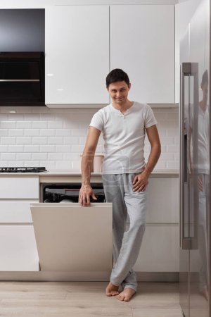Foto de Marido guapo hombre usando lavavajillas y lavando platos en la cocina moderna blanca - Imagen libre de derechos
