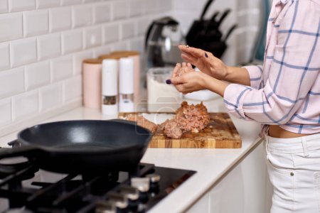 Foto de Mujer preparando chuletas de carne en cocina blanca - Imagen libre de derechos