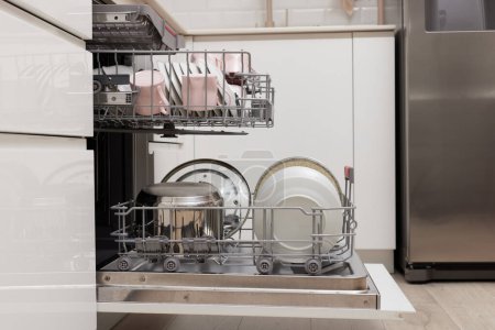 Photo for Open built-in dishwasher machine with clean cutlery, dishes, plates in white modern kitchen. side view - Royalty Free Image