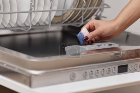 Téléchargez les photos : Main féminine met la tablette de lave-vaisselle dans la machine à lave-vaisselle intégrée automatique ouverte avec plat sale à l'intérieur dans la cuisine - en image libre de droit
