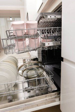 Foto de Lavavajillas empotrado abierto con cubiertos limpios, platos, platos en la cocina moderna blanca - Imagen libre de derechos