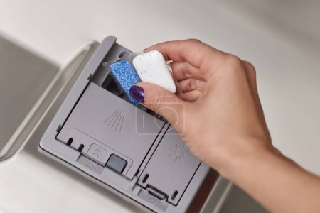 Téléchargez les photos : Main femelle met la tablette de lave-vaisselle dans la machine à lave-vaisselle intégrée automatique ouverte. Gros plan - en image libre de droit