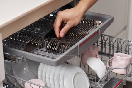 Téléchargez les photos : Cuillère de déchargement à la main mâle de la machine à laver le vaisselle automatique ouverte avec des ustensiles propres à l'intérieur - en image libre de droit
