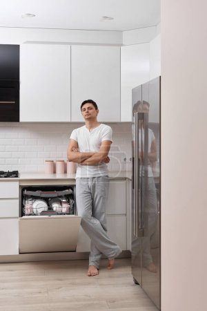 Téléchargez les photos : Beau mari homme utilisant lave-vaisselle et lave-vaisselle dans la cuisine moderne blanche - en image libre de droit