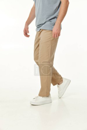 Téléchargez les photos : Homme portant des baskets blanches et un pantalon décontracté beige sur fond de studio. vue latérale - en image libre de droit