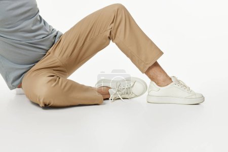 Téléchargez les photos : Homme portant des baskets blanches et un pantalon beige assis sur le sol - en image libre de droit