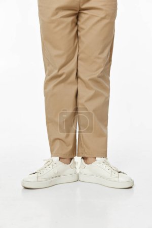 Téléchargez les photos : Homme portant des baskets blanches et un pantalon décontracté beige sur fond studio, vue de face - en image libre de droit