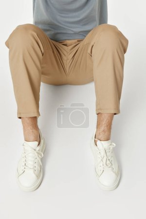 Téléchargez les photos : Homme portant des baskets blanches et un pantalon beige assis sur le sol - en image libre de droit