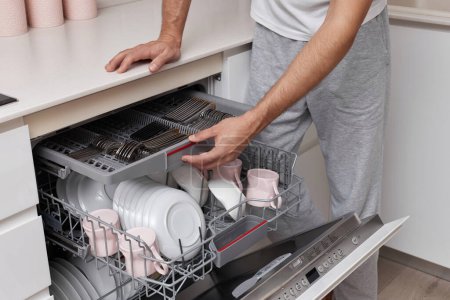 Téléchargez les photos : Gros plan, homme charge des plaques dans la machine à laver le vaisselle dans la cuisine - en image libre de droit