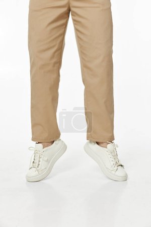 Téléchargez les photos : Homme portant des baskets blanches et un pantalon décontracté beige sautant sur fond studio, vue de face - en image libre de droit