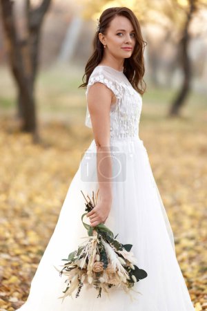 Photo for Beautiful happy bride holding wedding autumn bouquet in nature - Royalty Free Image