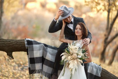 Foto de Hermosa feliz novia y novio con estilo en el sombrero cerca del árbol en otoño - Imagen libre de derechos