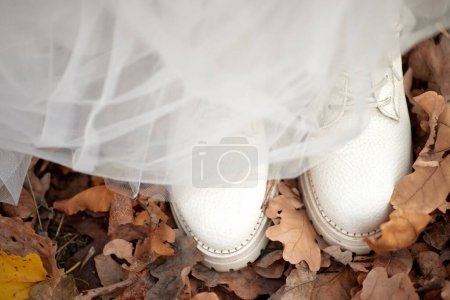 Photo for Bride wearing white boots and white dress is standing on fall leaves. autumn wedding - Royalty Free Image