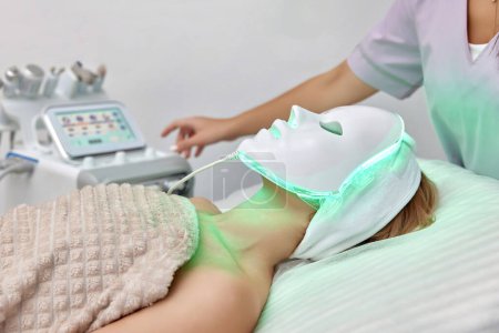 woman getting cosmetic procedure with LED facial mask in beauty salon