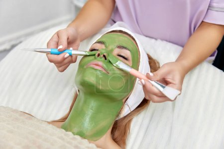 Photo for Female beautician applies the mask to the face of beautiful woman in the spa salon. facial skin care - Royalty Free Image