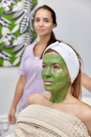 Téléchargez les photos : Femme cosmétologue et cliente avec masque facial en clinique de beauté. - en image libre de droit