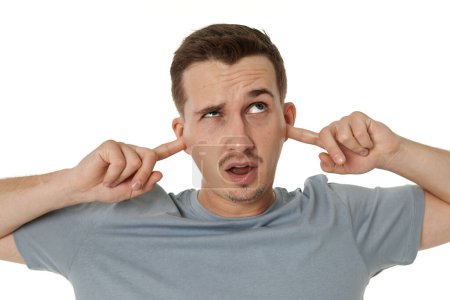 Foto de Joven hombre caucásico molesto en camiseta cubre las orejas con las manos dedos sobre fondo blanco - Imagen libre de derechos