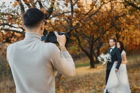 Foto de Fotógrafo de bodas profesional tomando fotos de la novia y el novio al aire libre en otoño - Imagen libre de derechos