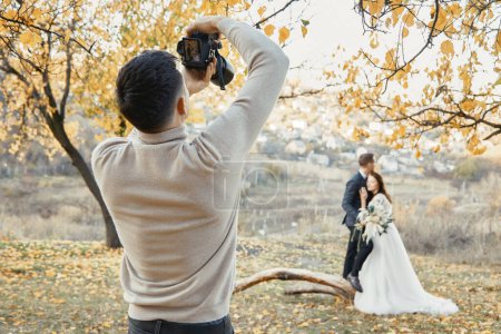 Foto de Fotógrafo de bodas profesional en acción. la novia y el novio en la naturaleza en otoño - Imagen libre de derechos