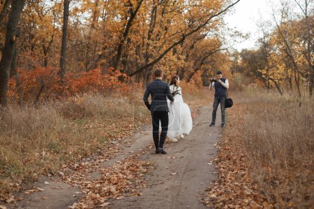 Photo for Professional wedding photographer taking pictures of the bride and groom in nature in autumn - Royalty Free Image