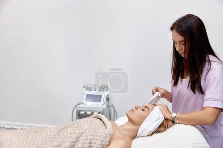 Téléchargez les photos : Cosmetologue mettre serviette bandeau blanc sur la tête de la patiente dans le salon de beauté - en image libre de droit