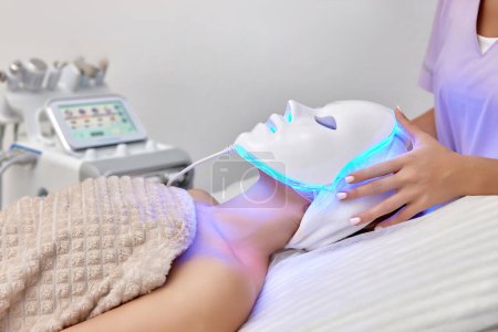 Photo for Woman receiving led light anti-aging mask treatment from beautician in beauty salon - Royalty Free Image