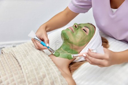 Téléchargez les photos : Esthéticienne féminine applique le masque sur le visage de la belle femme dans le salon de spa. soin du visage - en image libre de droit