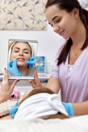 Foto de Hermosa mujer se mira en el espejo después del procedimiento aumento de labios en la clínica médica de belleza. - Imagen libre de derechos