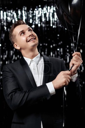 Photo for Happy handsome man in black jacket holding black air balloons on glitter background. - Royalty Free Image