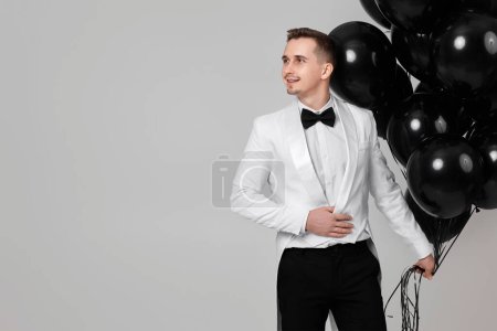 Foto de Elegante hombre caucásico en traje blanco esmoquin con manojo de globos de aire negro. espacio de copia - Imagen libre de derechos