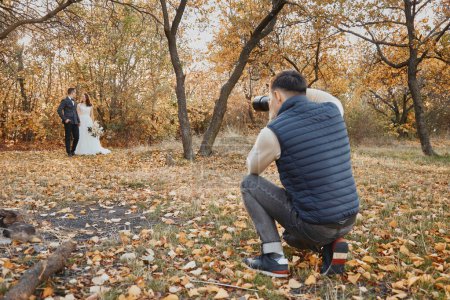 Photo for Male wedding photographer taking pictures of the bride and groom in nature in autumn - Royalty Free Image