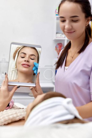 Foto de Hermosa mujer se mira en el espejo después del procedimiento aumento de labios en la clínica médica de belleza. - Imagen libre de derechos
