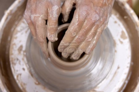 Téléchargez les photos : Mains masculines faisant tasse en céramique sur roue de poterie, Gros plan, vue de dessus. homme faisant tasse à partir pot d'argile - en image libre de droit