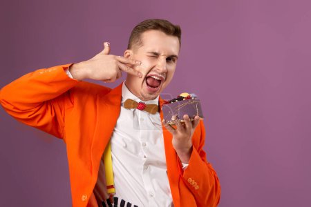 Photo for Funny guy in orange jacket eating cake on purple background - Royalty Free Image