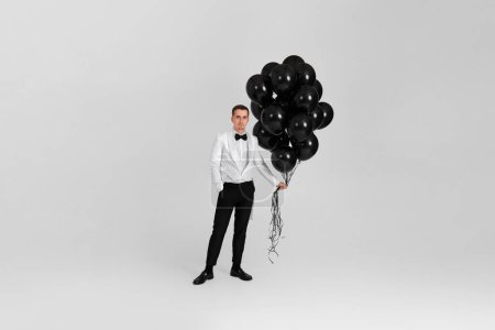 Foto de Elegante hombre caucásico en traje esmoquin blanco con globos de aire negro sobre fondo blanco. Longitud total. fiesta de cumpleaños - Imagen libre de derechos