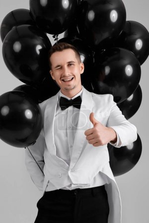 Téléchargez les photos : Élégant homme caucasien en costume blanc smoking avec ballons à air noir sur fond blanc. - en image libre de droit