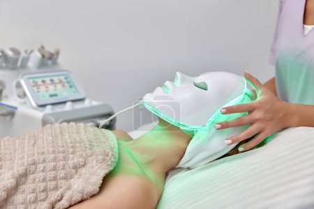 Téléchargez les photos : Femme recevant le traitement mené de masque de luminothérapie de l'esthéticienne dans le salon de beauté - en image libre de droit