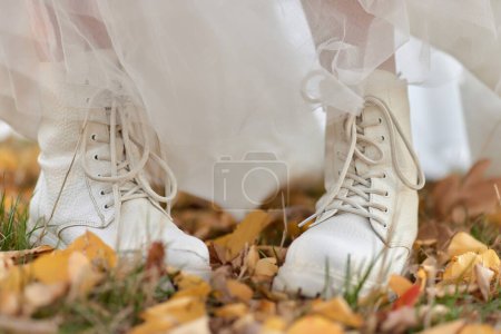 Foto de Novia con botas blancas y vestido blanco está de pie sobre hojas de otoño. boda de otoño - Imagen libre de derechos
