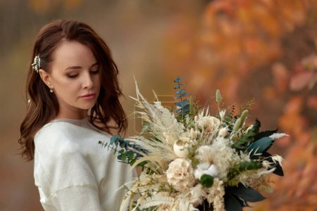 Téléchargez les photos : Portrait de belle mariée heureuse tenant mariage bouquet d'automne dans la nature - en image libre de droit