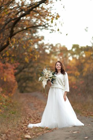 Téléchargez les photos : Belle mariée heureuse tenant mariage bouquet d'automne dans la nature - en image libre de droit