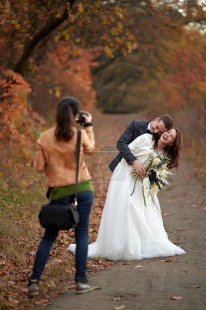 Photo for Female wedding photographer taking pictures of the bride and groom in autumn - Royalty Free Image