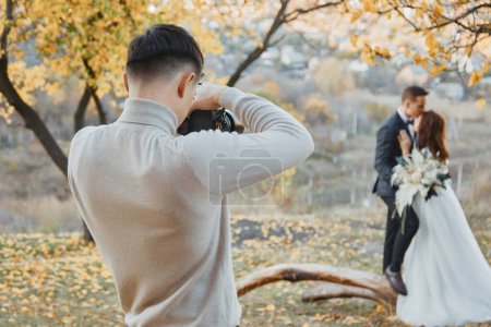 Photo for Professional wedding photographer taking pictures of the bride and groom in nature in autumn - Royalty Free Image