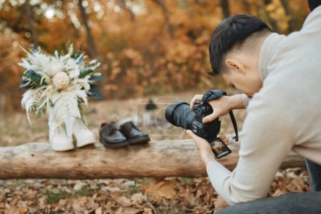 Foto de Fotógrafo de boda tomando fotos de los zapatos de novia y novio, ramo de boda al aire libre. - Imagen libre de derechos